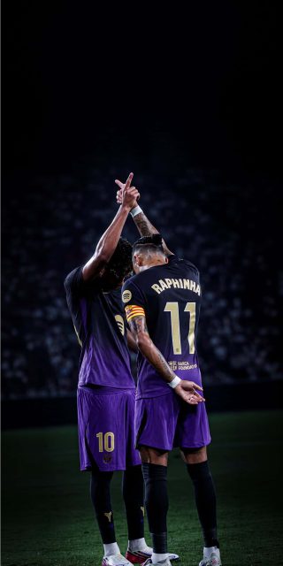 FC Barcelona football players Raphinha and Lamine Yamal celebrating on the field in purple kits under stadium lights.