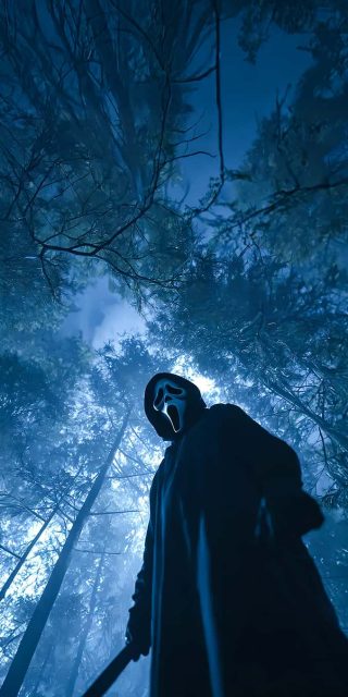Low-angle view of Ghostface holding a knife in a dark, misty forest looking up toward towering tree branches under moonlight