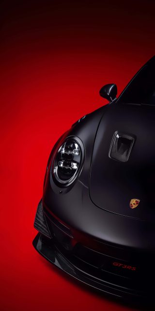 Close-up front view of a matte black Porsche 911 GT3 RS headlights and carbon fiber hood on a vibrant red background